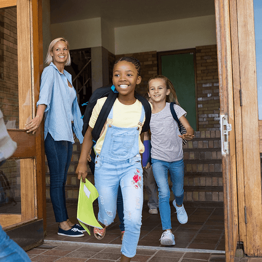 A smiling teacher holding the door open for happy students