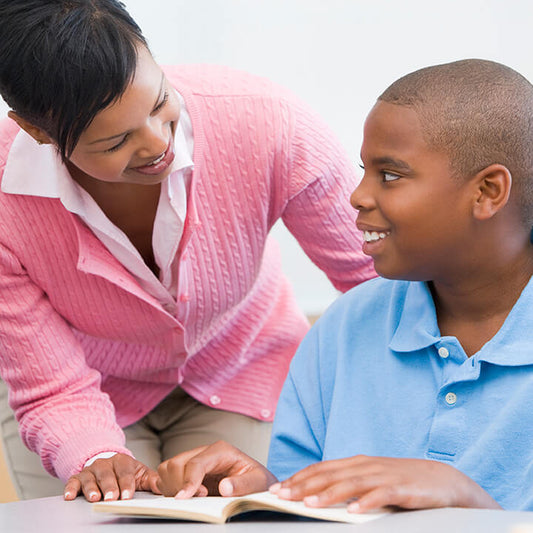 Smiling teacher and student with open book on desk