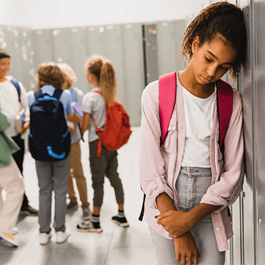 A sad looking student leaning against a locker in the hallway